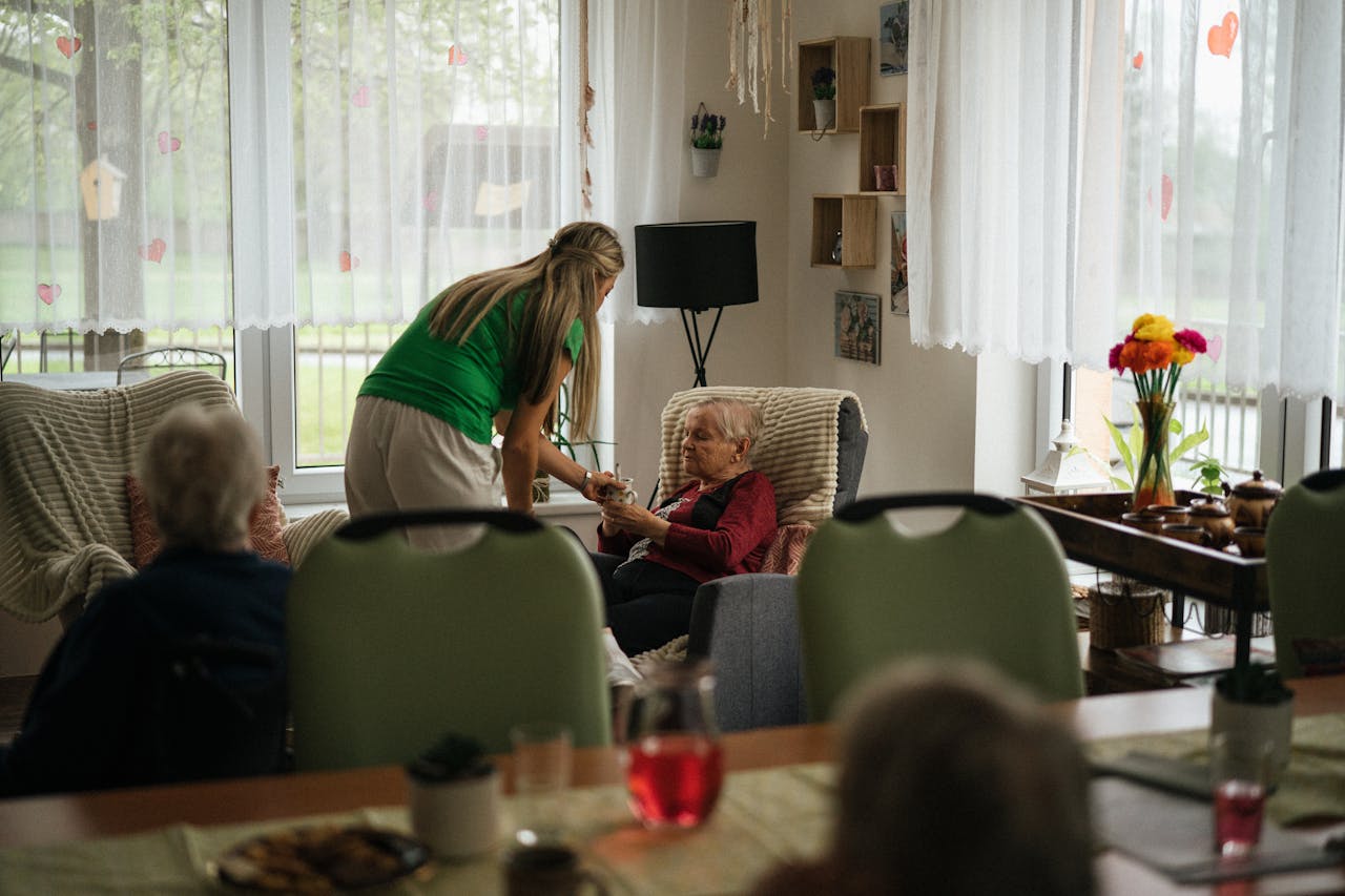 Home Caregiver assisting elderly women with tea in a cozy nursing home setting.